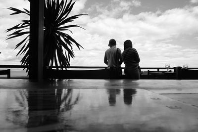 Rear view of couple walking by swimming pool against sky