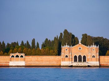 Built structure by river against clear blue sky