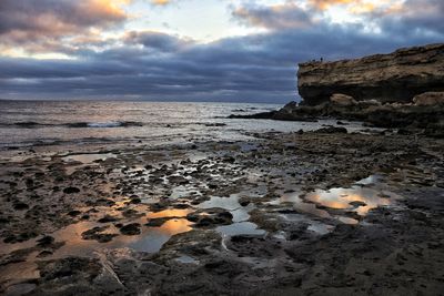 Rocks on beach against sky during sunset