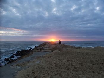 Silhouette man standing on beach against sky during sunset