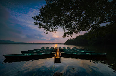 Deck chairs by swimming pool against sky during sunset