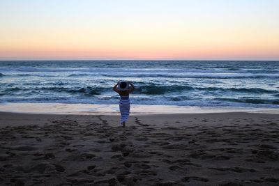 Rear view of young woman walking at beach during sunset