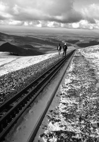 People on railroad tracks by sea against sky