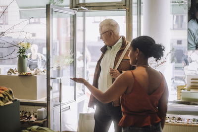 Rear view of female sales clerk gesturing while showing around to senior male customer