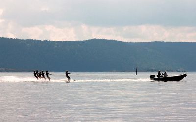 Silhouette people water skiing on sea against sky