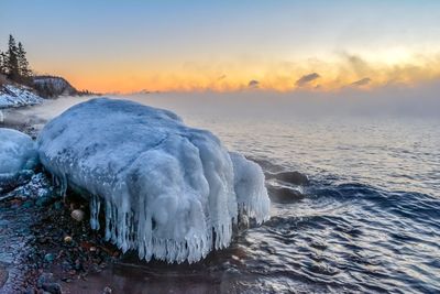 Frozen sea against sky during sunset