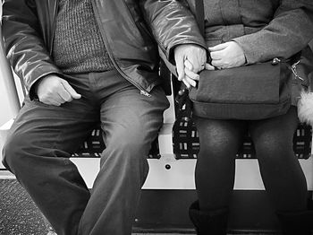 Midsection of couple holding hands while sitting in metro train