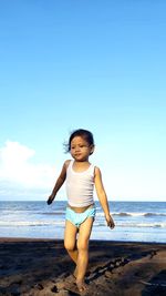 Rear view of girl standing at beach against blue sky