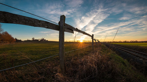 Railroad tracks on field against sky during sunset