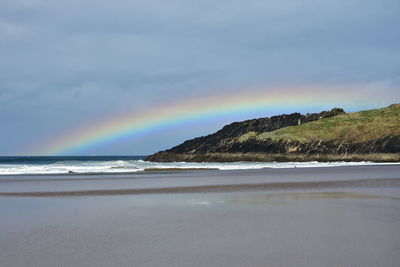 Scenic view of beach against rainbow in sky