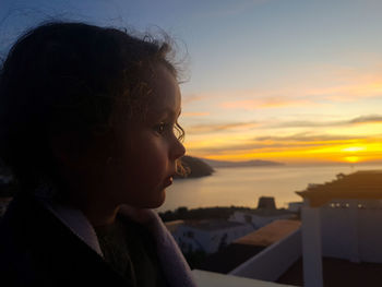 Close-up portrait of boy looking at sea against sky during sunset