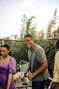 Young man laughing while celebrating with friends at party in back yard