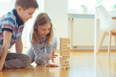 Siblings playing with toy blocks on floor at home