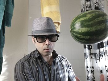 Man wearing hat and eyeglasses looking at watermelon levitating