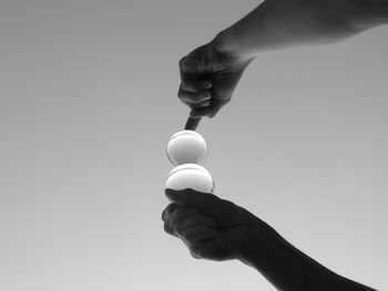 Low angle view of person balancing crystal balls against clear sky