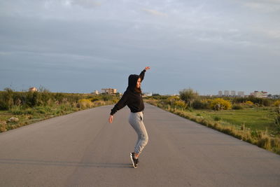 Rear view of man jumping on road against sky