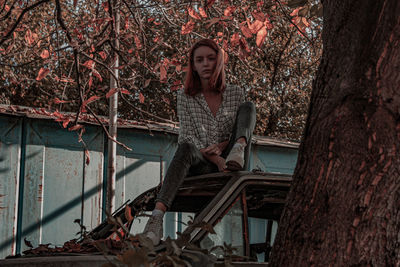 Portrait of young woman sitting on tree trunk