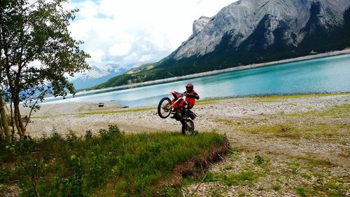 Man riding motorcycle at lakeshore against mountain