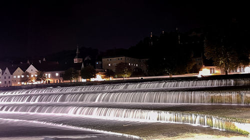 Illuminated city by river against clear sky at night