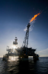 Oil rig in sea emitting fire on sunny day