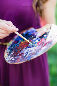 Midsection of woman holding palette and paintbrush