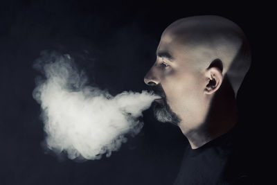 Close-up of young man smoking against black background