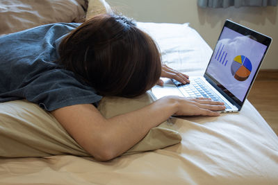 Rear view of woman using mobile phone on bed