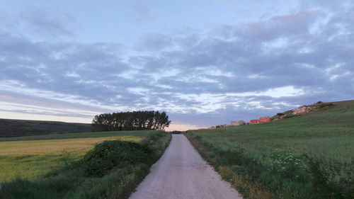 Road passing through field against cloudy sky