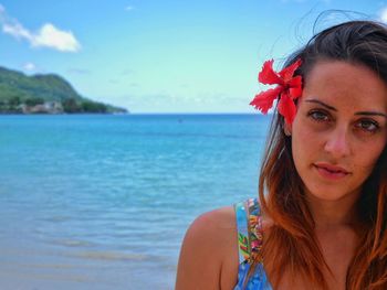 Portrait of woman wearing red flower against sea