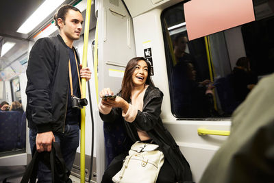 Happy woman holding mobile phone while sitting by man in train