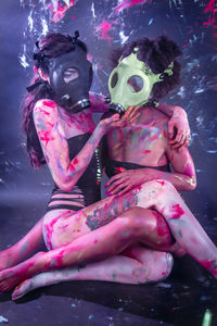 Young women wearing bikini while face covered with gas mask sitting at nightclub 