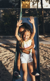 Friendly active diverse girls having fun at slide in bright day