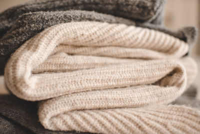 Stack of knitted wool textile sweaters clothes on white blanket in bed at home room close up.