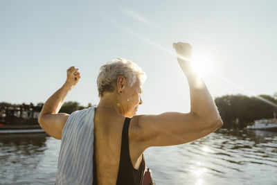 Senior woman flexing muscles on houseboat during vacation at sunny day