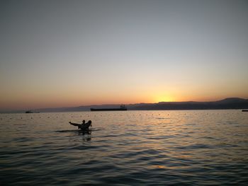 Silhouette man lifting woman in sea against clear sky