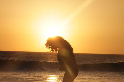 Side view of woman on beach against sky during sunset