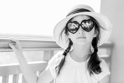 Portrait of girl wearing sunglasses and hat standing by railing