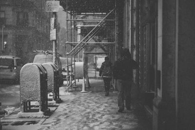 Rear view of people walking on sidewalk by building during snowfall