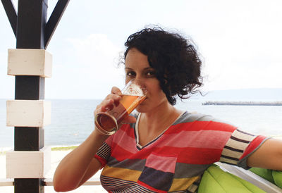 Portrait of woman drinking alcoholic drink while sitting against sea