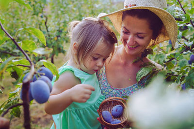 Mother and daughter picking fruit from tree