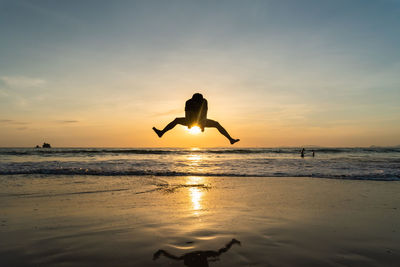 Silhouette people jumping on beach against sky during sunset