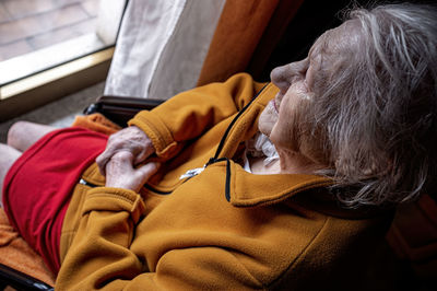 Elderly woman in a wheelchair looking out the window with a sad and suffering look