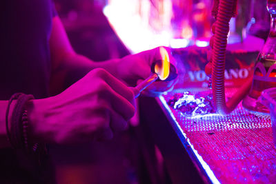 Midsection of man burning coal by hookah in illuminated nightclub