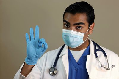 Close-up portrait of doctor gesturing ok sign against gray background