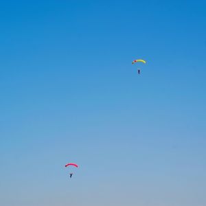 Low angle view of people paragliding against clear blue sky