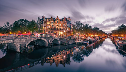 Scenic wide shot of boats moored in canal by bridge at night