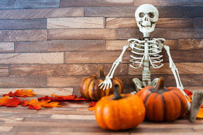 Pumpkins and skull amidst dry leaves on hardwood floor