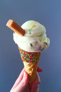 Cropped image of woman holding ice cream cone against blue background