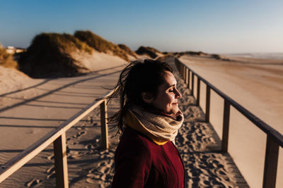 Portrait of young woman standing on railing against sky