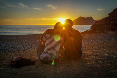 Rear view of men sitting on beach during sunset